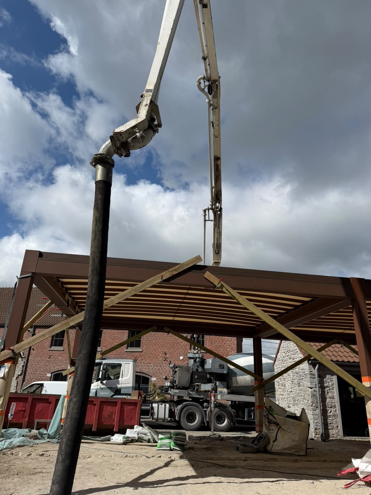 Grue hydraulique déployée sur chantier, bras métallique au-dessus d’une charpente en bois, ciel nuageux.